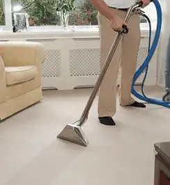 Professional carpet cleaner using a hot-water extraction wand and hose machine in a living room in Jackson, MS.