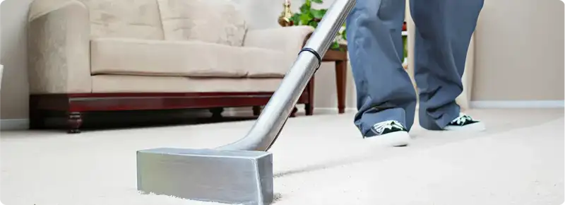 Carpet cleaning technician using a hot-water extraction wand on a light-colored carpet in a living room, Jackson, MS.