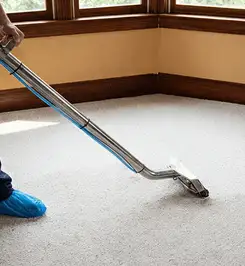Steam carpet cleaning technician using a hot-water extraction wand on a residential carpet, wearing blue protective shoe covers Jackson, MS.