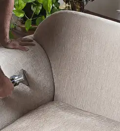 Professional upholstery cleaner deep-cleaning a fabric sofa with a handheld extraction tool and hose Jackson, MS.