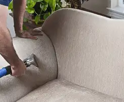Professional upholstery cleaner deep-cleaning a fabric sofa with a handheld extraction tool and hose in Jackson, MS.